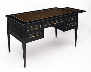 Desk, French, in the Louis XVI style made of ebonized Mahogany that has been finished in a lustrous museum quality French polish. This work table boasts a gilt embossed brown leather top and four dovetailed drawers. The original hardware and gilt brass trims can be found throughout. It is supported by fluted and tapered legs. There is one pull out leaf that adds an additional 15” to the length.