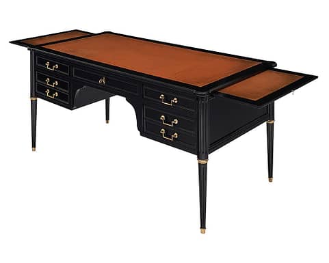 Desk, French, in the Louis XVI style with the original leather top and striking tapered and fluted legs. The important desk features ample storage inside the dovetailed drawers and additional pull out extension tablets. Each leaf/tablet adds an additional 16.5” of length to the desk. One drawer has an easy glide pull added for functionality. It has been finished in a lustrous ebonized French polish. Brass pulls adorn the backside of the desk for a “faux” partner desk appearance. The heartthrob of interior design.